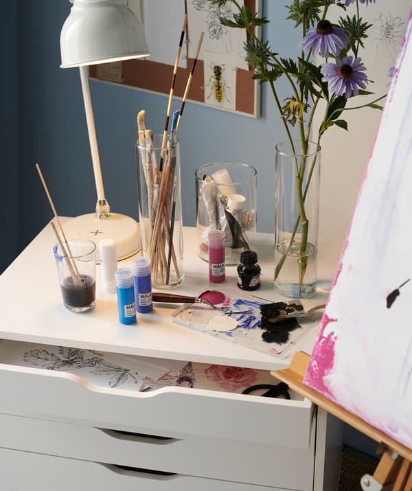 A white ALEX drawer unit on casters doubling as both a place to store paintings and a charging station for electronics