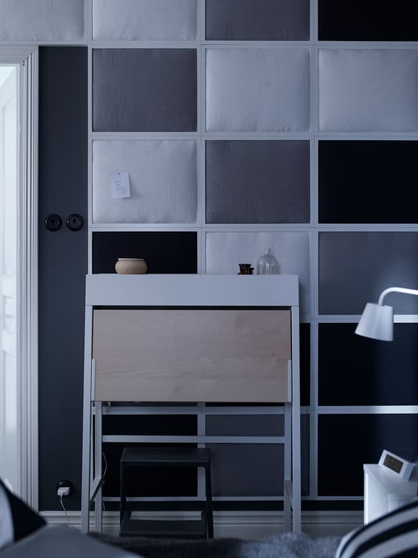 A white and birch IKEA PS bureau paired with white side tables and lamps in a bedroom.