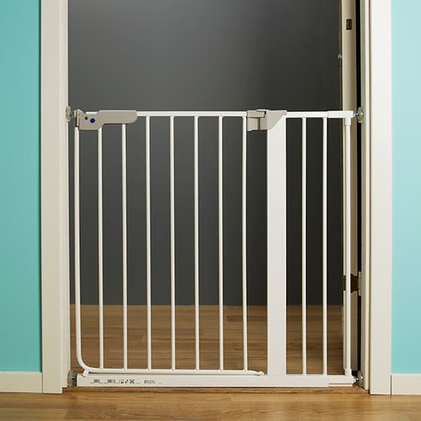 A white baby safety gate wedged into a doorway with a brown wood floor.