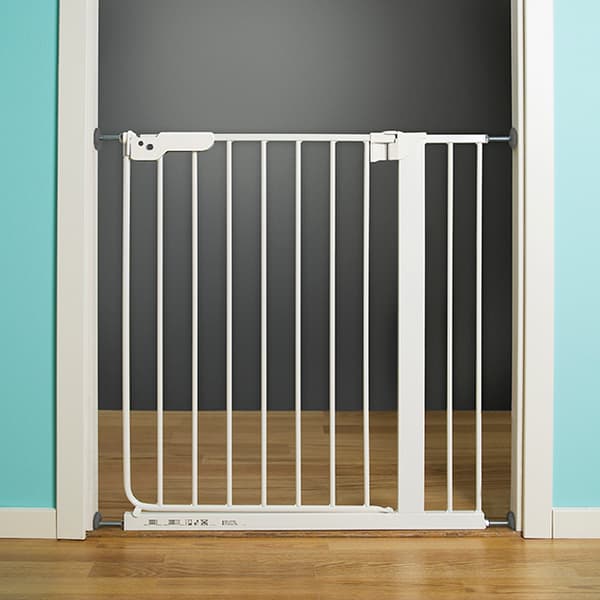 A white baby safety gate wedged into a doorway with a brown wood floor.