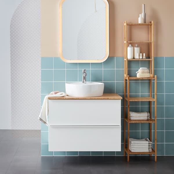 A white bathroom cabinet with a round counter top wash-basin, next to a bamboo shelving unit. 