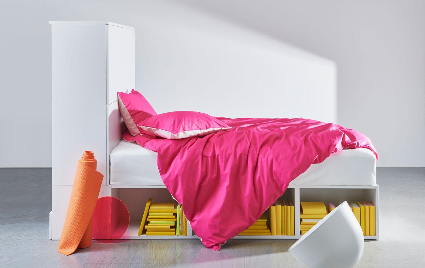 A white bed frame with built-in storage dressed with pink bedding.