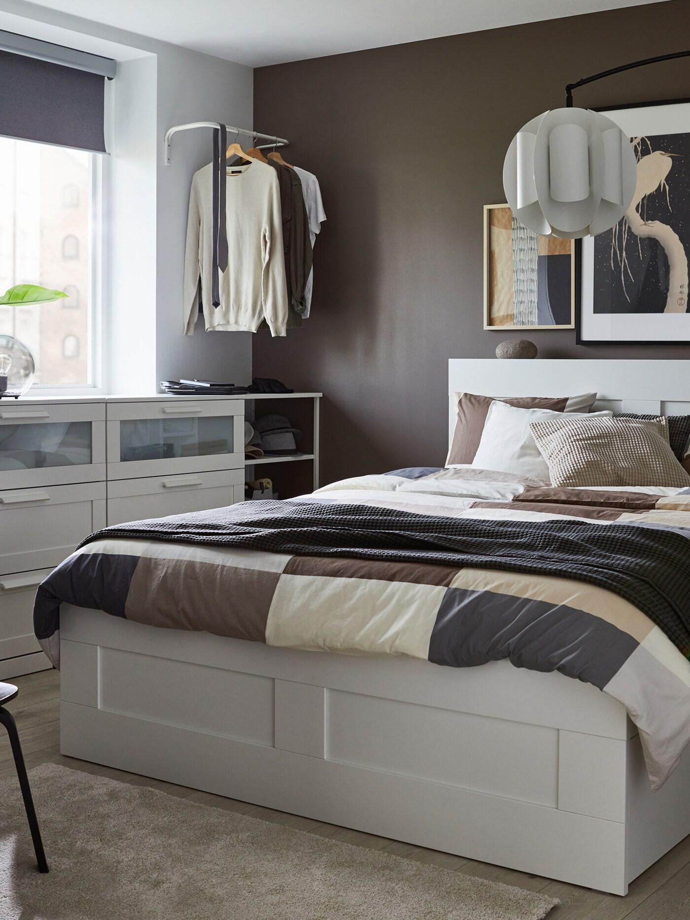 A white bed with headboard, brown patterned quilt cover and pillow cases, grey throw and cushions in white, grey and beige.