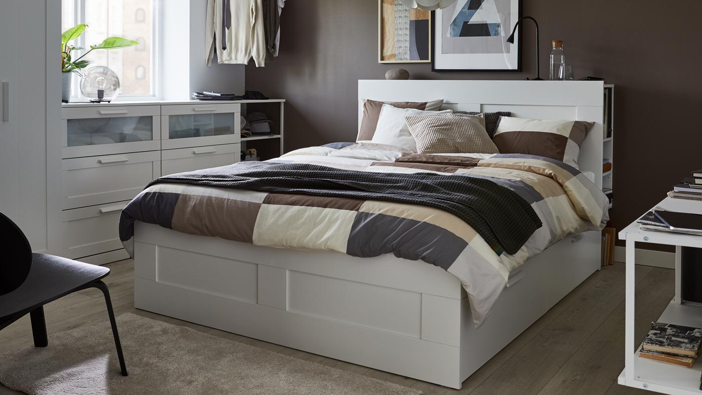 A white bed with headboard, brown patterned quilt cover and pillow cases, gray throw and cushions in white, gray and beige.