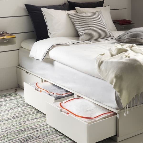 A white bedframe with storage drawers below open to show storage bags inside.
