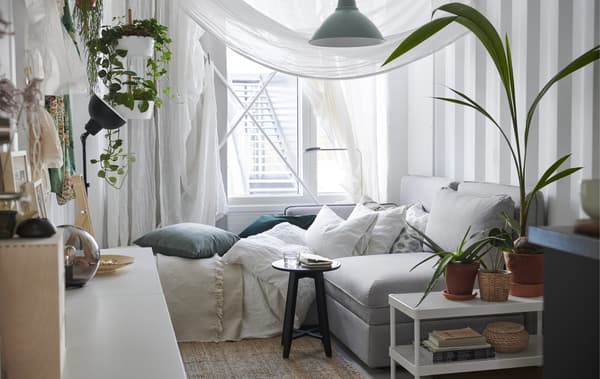 A white bedroom with neutral textiles, sheer curtains draped around the sofa bed and pot plants.