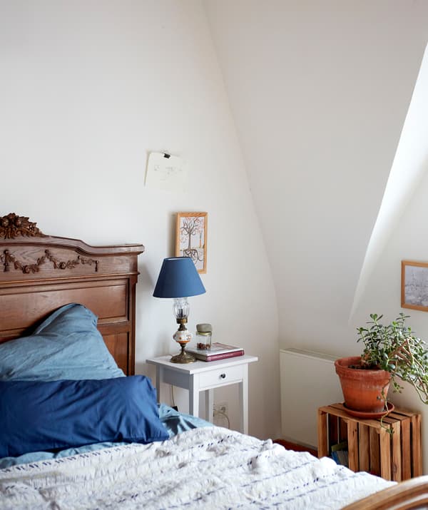 A white bedroom with pitched ceiling, dark wooden bed with blue bedding and white HEMNES bedside table.