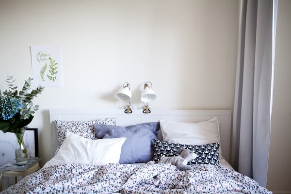 A white bedroom with two lamps clamped on the bed frame.
