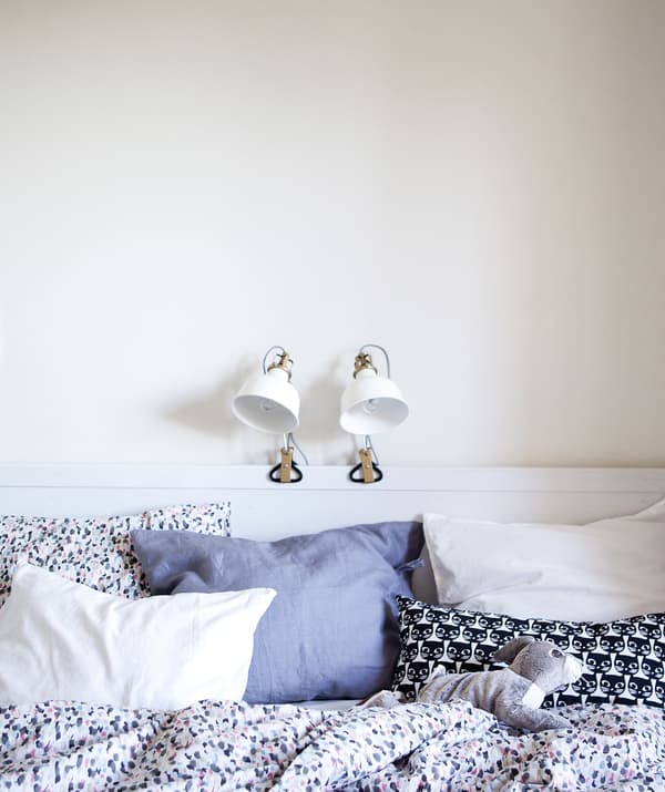 A white bedroom with two lamps clamped on the bed frame.