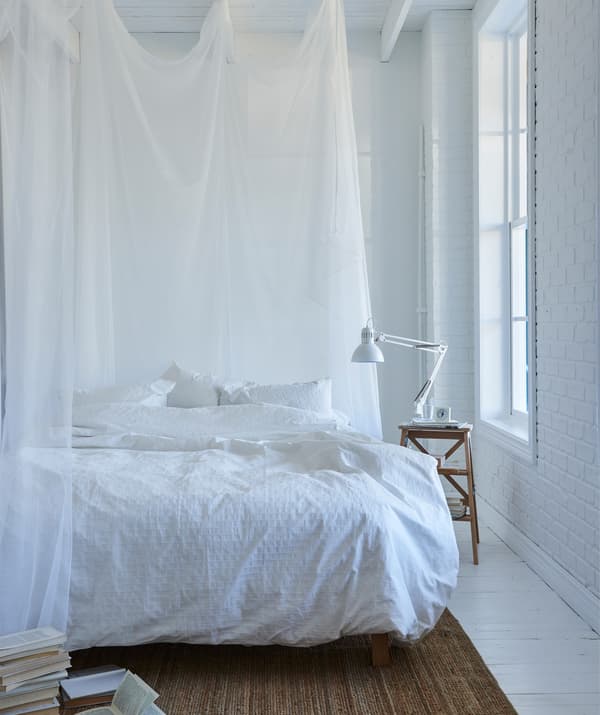 A white bedroom with white bedding and sheer white curtains around the bed.