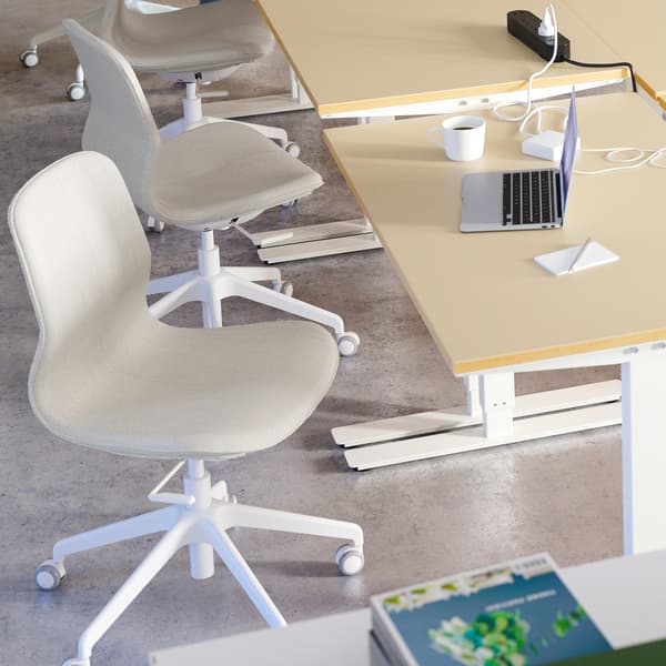 A white/beige desk and a white/beige chair standing next to several desks, a laptop and a white coffee mug.