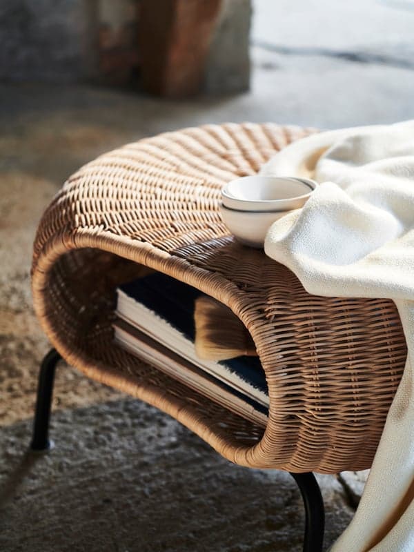 A white blanket and three white bowls on a GAMLEHULT footstool with books stored inside.