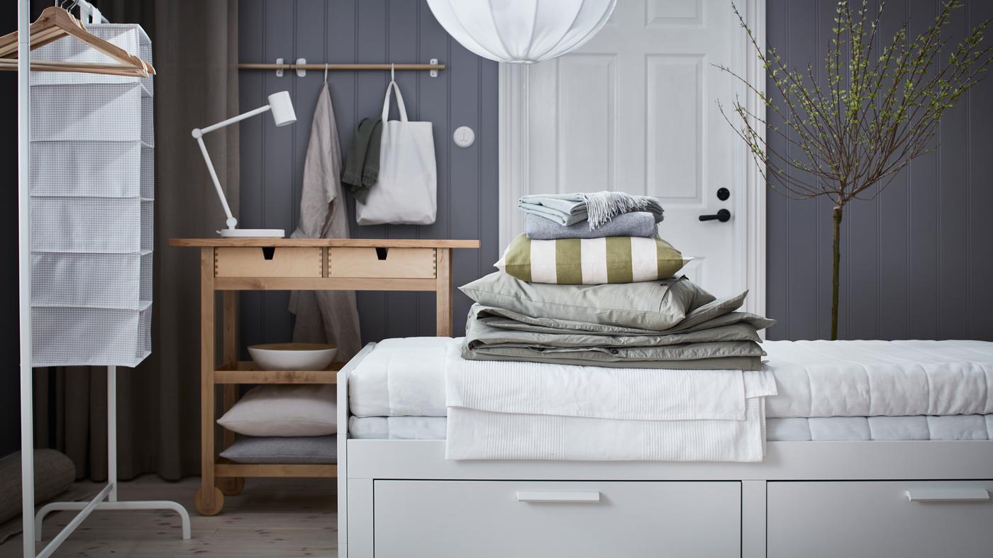 A white BRIMNES day-bed with 2 drawers stands in a room in front of a door and a FÖRHÖJA kitchen trolley.