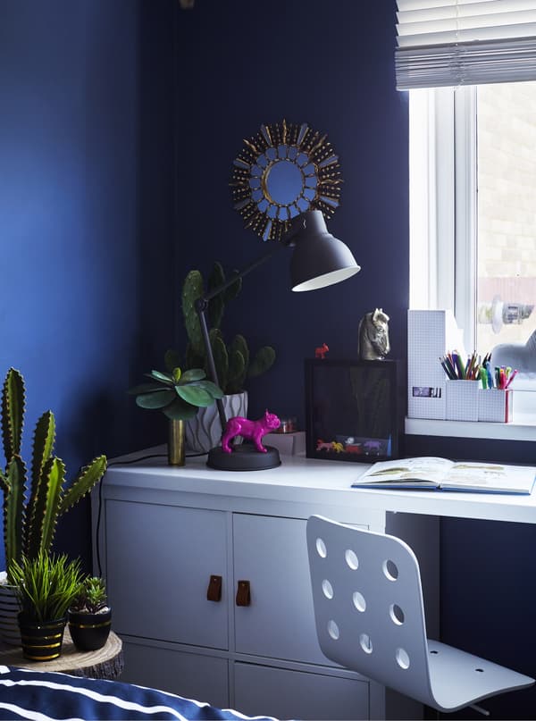 A white children's desk with a white circular cut-out desk chair and white storage cabinet, placed up against a windowsill.