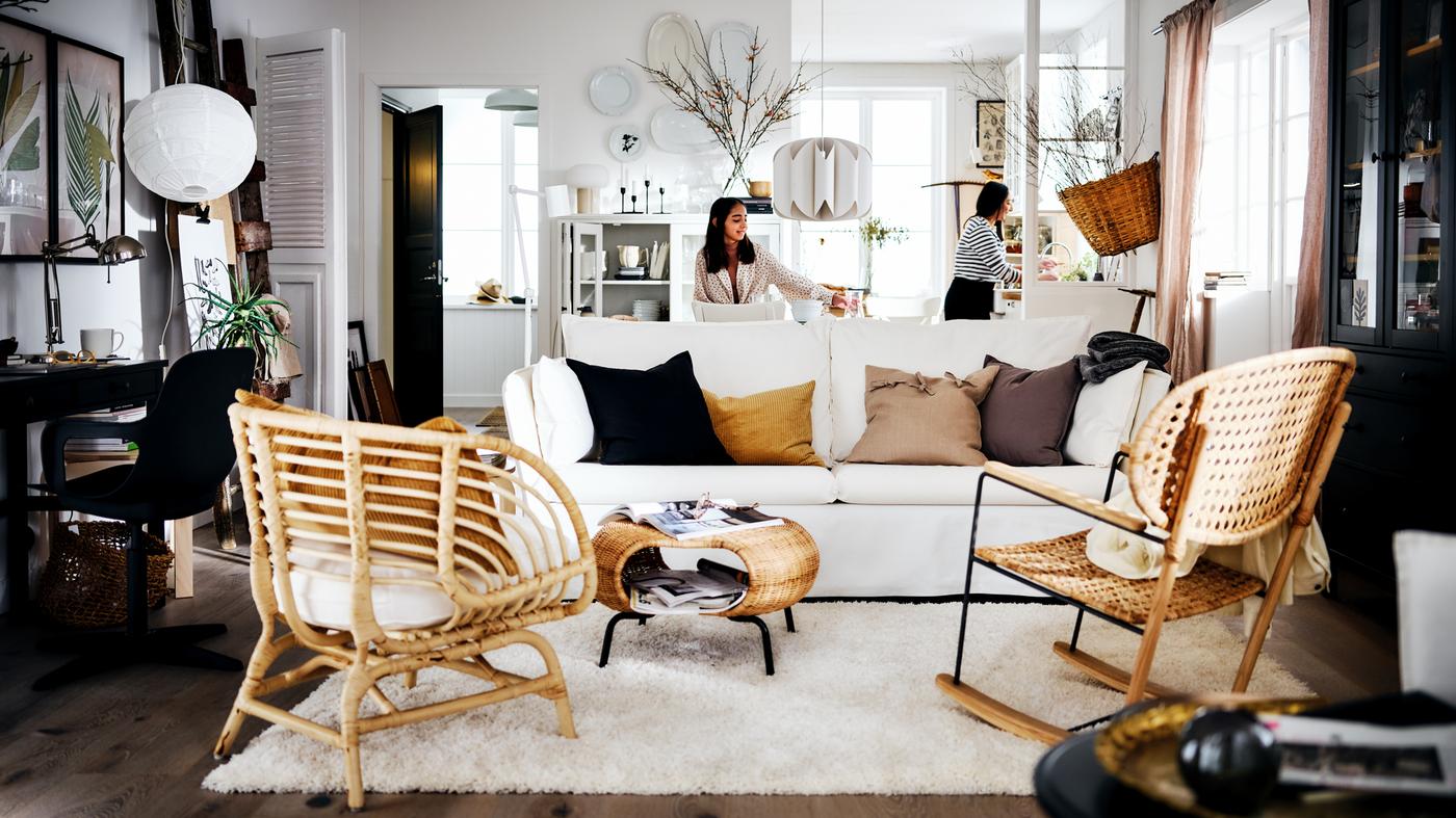 A white country-style living area with two women behind a white BACKSÄLEN sofa that’s in front of a rug and two armchairs.