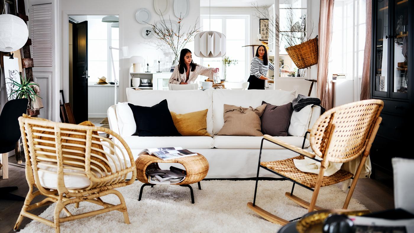A white country-style living area with two women behind a white BACKSÄLEN sofa that’s in front of a rug and two armchairs.