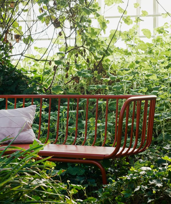 A white cushion on a red bench surrounded by greenery.