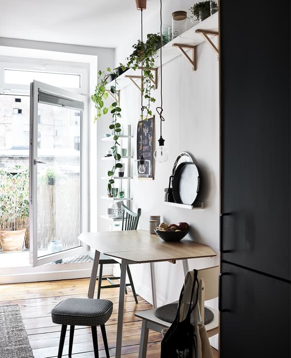 A white dining area with plants on a shelf above and an open door.