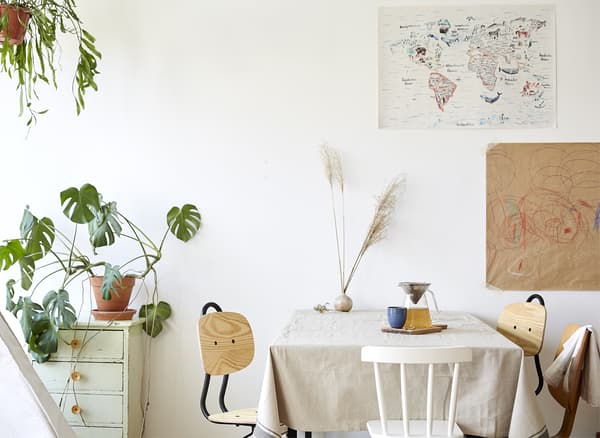 A white dining area with wooden chairs and a large Swiss cheese plant.