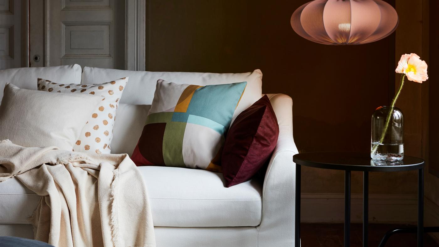 A white FÄRLÖV sofa with different cushions and a throw sits near a black table and a REGNSKUR pendant lamp.