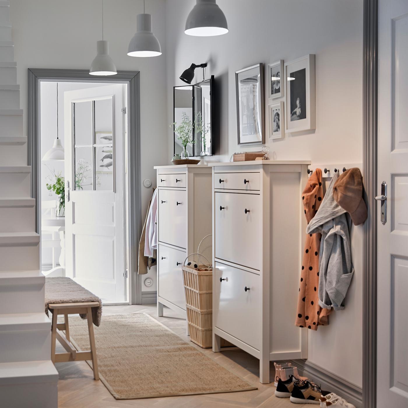 A white hallway with two traditional white HEMNES shoe cabinets side by side and a row of hooks for coats.