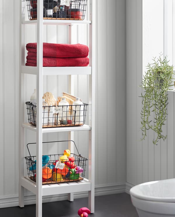 A white HEMNES shelf unit with black PLEJA wire baskets storing towels, bath toys, spa stuff and more on the four shelves.