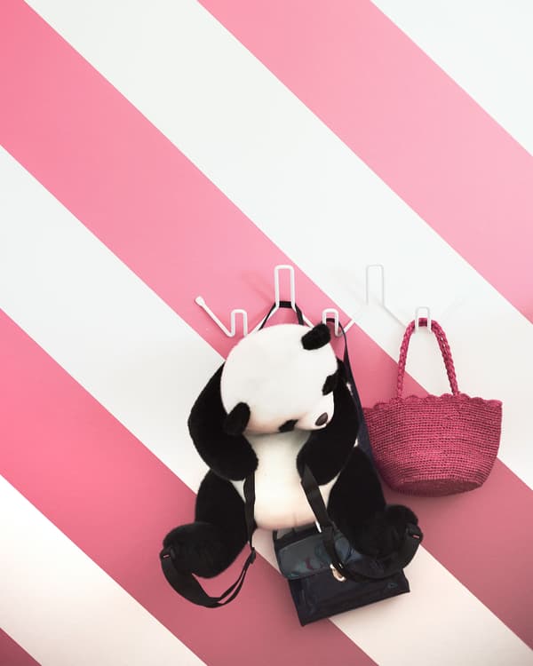 A white hook unit mounted to the wall against a pink and white striped wall, holding a pink purse and panda plush.