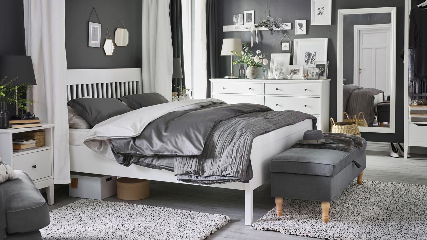 A white IDANÄS bed, bedside table and chest of drawers stand in a bedroom, with LUKTJASMIN bed linen on the bed.