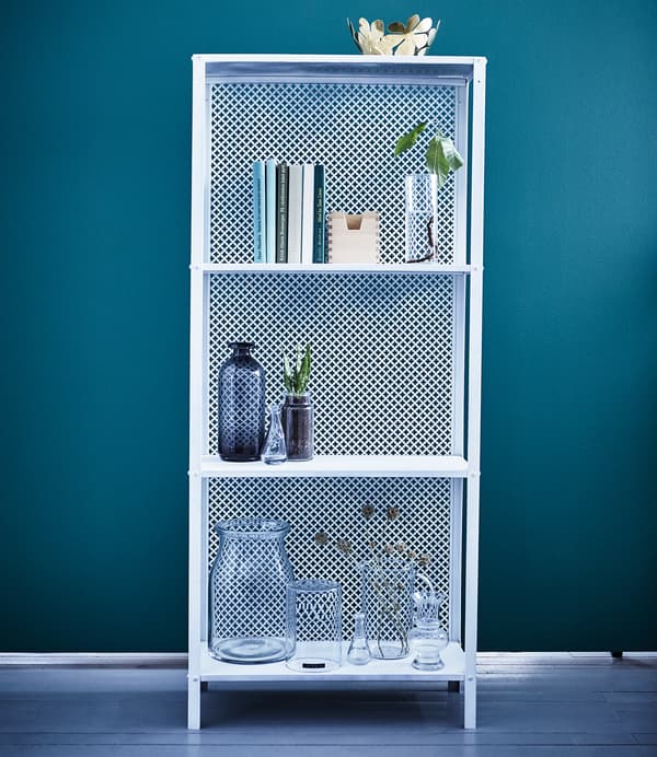 A white IKEA HYLLIS shelving unit is decorated with books, plants, and glass vases.