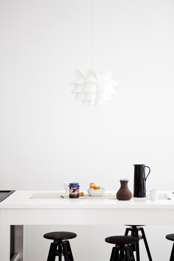 A white kitchen with countertop, black stools and white pendant lampshade.