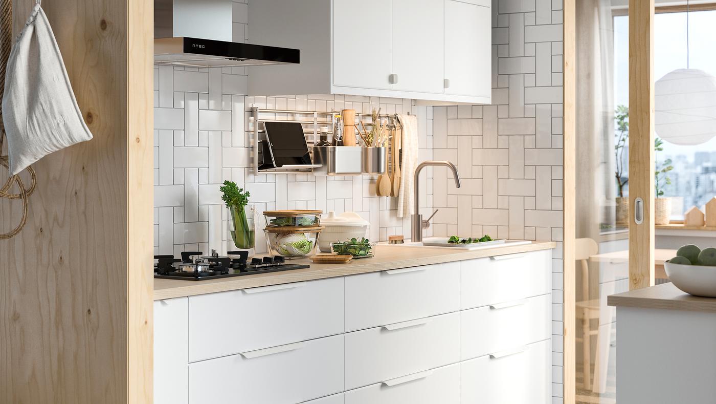 A white kitchen with KUNGSBACKA white drawers below a pale wood worktop and a white wall cabinet above.