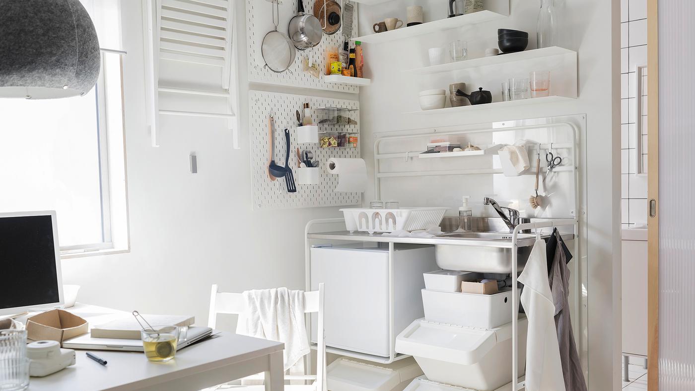 A white kitchenette with the white SUNNERSTA mini-kitchen, a small white fridge, a white table and one white chair.