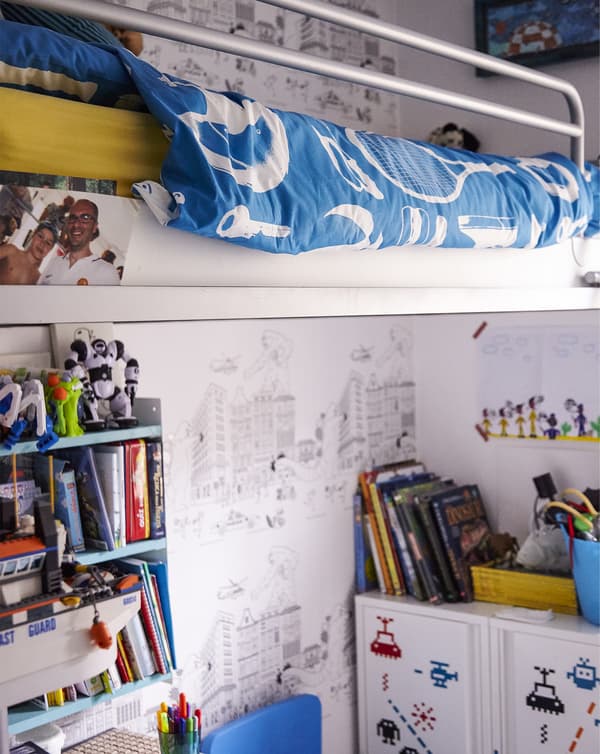 A white loft bed in a child’s bedroom, with books, shelving, and storage underneath.