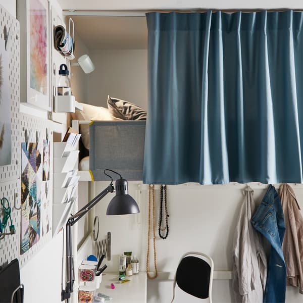 A white loft bed that is mostly covered by a blue curtain that's attached to a curtain track in the ceiling.