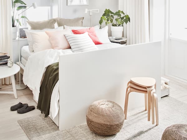 A white MALM double bed, made with many pillows and cushions and having its headboard as foot end, stands in a bright room.