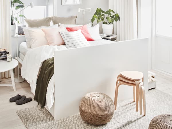 A white MALM double bed, made with many pillows and cushions and having its headboard as foot end, stands in a bright room.