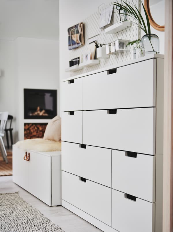 A white NORDLI chest of drawers standing against a white wall near the hallway area of an open floor-plan home interior.