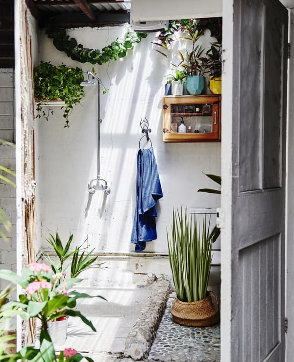 A white outdoor shower room with lots of plants.