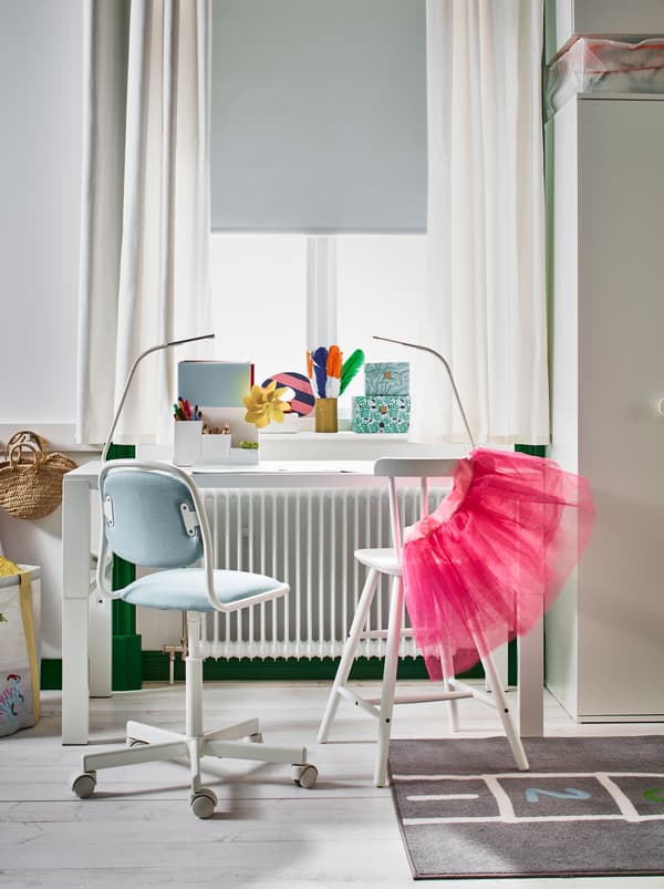 A white PÅHL desk and AGAM junior chair placed next to a sunlit window in a light, wood-floor children’s room.