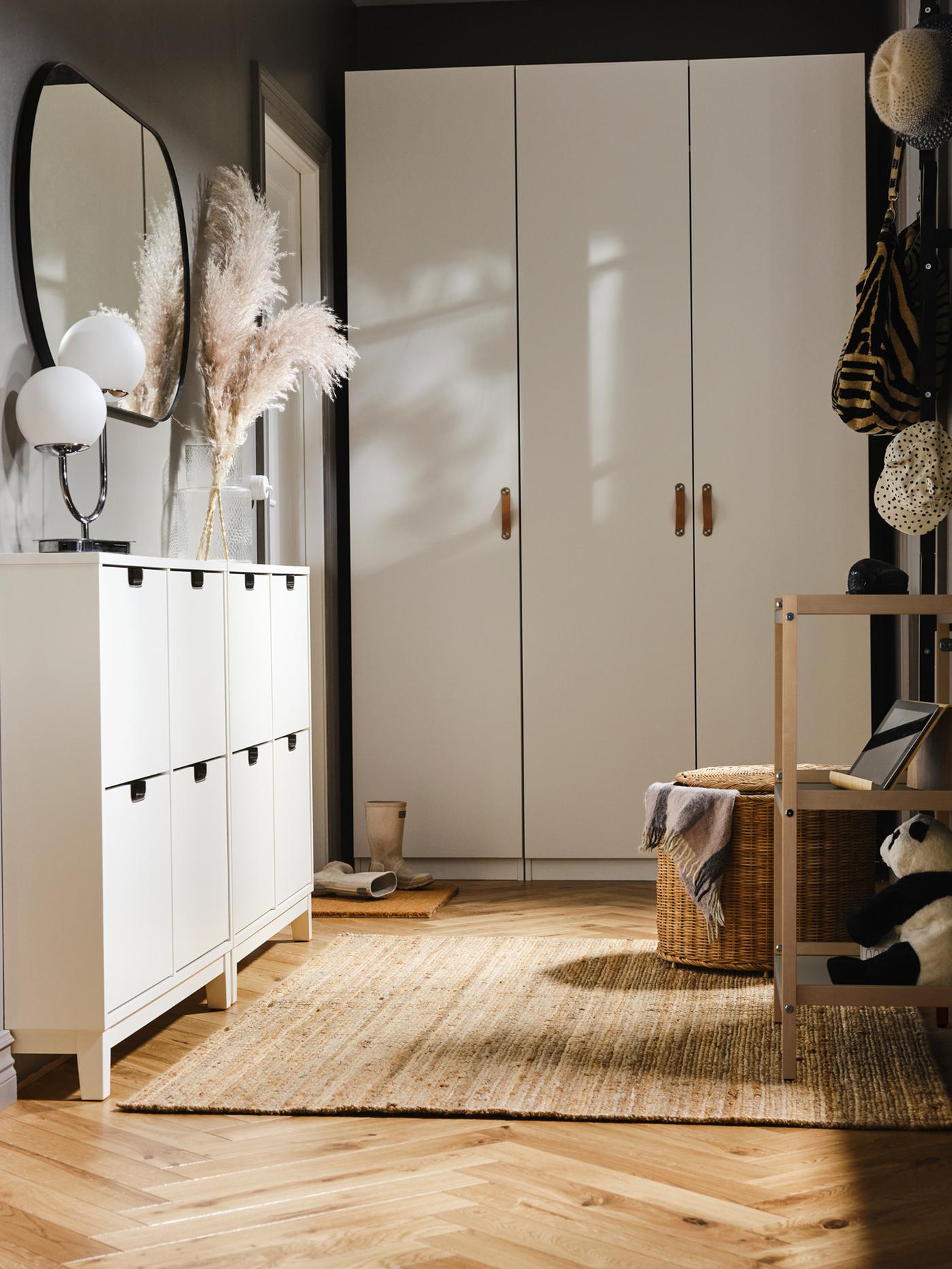A white PAX/FORSAND wardrobe at the end of a hallway, with two white STÄLL shoe cabinets on one side with a mirror above it.