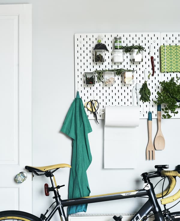A white pegboard filled with tools and plants in a white room.
