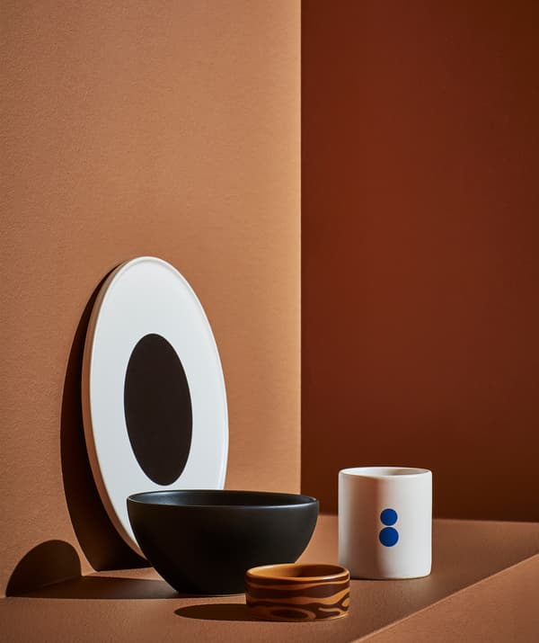 A white plate with black center, large black bowl, small brown bowl and white mug on an orange step.