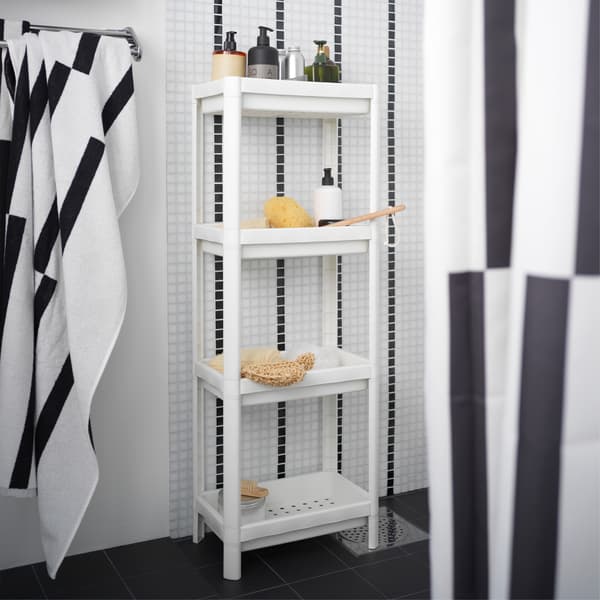 A white shelf unit is standing in a black/white shower and is storing shower necessities like shampoos and more.
