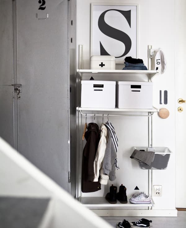 A white shelving unit in a hallway with boxes, and a low-level hanging rail and wire basket.