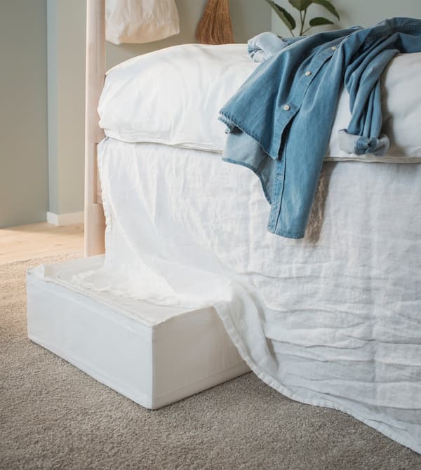 A white SKUBB storage case under a bed that’s hidden by an old curtain used as a bed skirt.