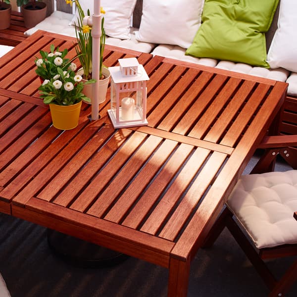 A white sofa with pillows and a square outdoor table made from brown acacia wood with decorations on top.