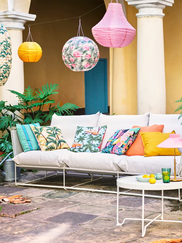 A white sofa with various coloured and patterned scatter cushions placed outside with a variety of hanging lanterns.