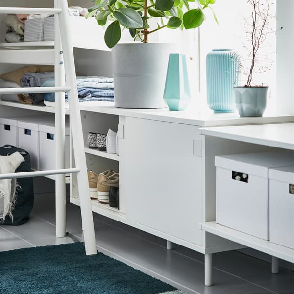 A white storage bench is placed by a loft bed ladder, and one of the opened sliding doors shows shoes stored inside.