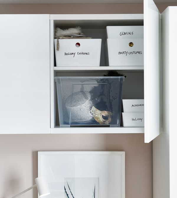 A white storage cabinet above a bed, opened to reveal labeled storage boxes within.
