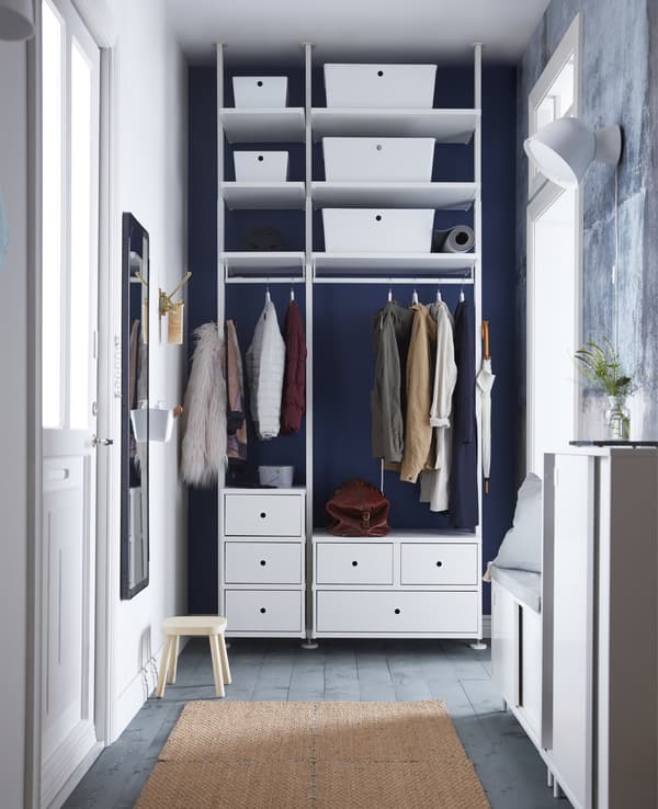 A white storage unit with clothes rail, shelves, and drawers, stretches from floor to ceiling in this narrow hall.